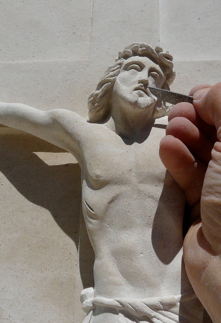 Main du sculpteur travaillant le visage d’un crucifix en pierre avec une râpe
